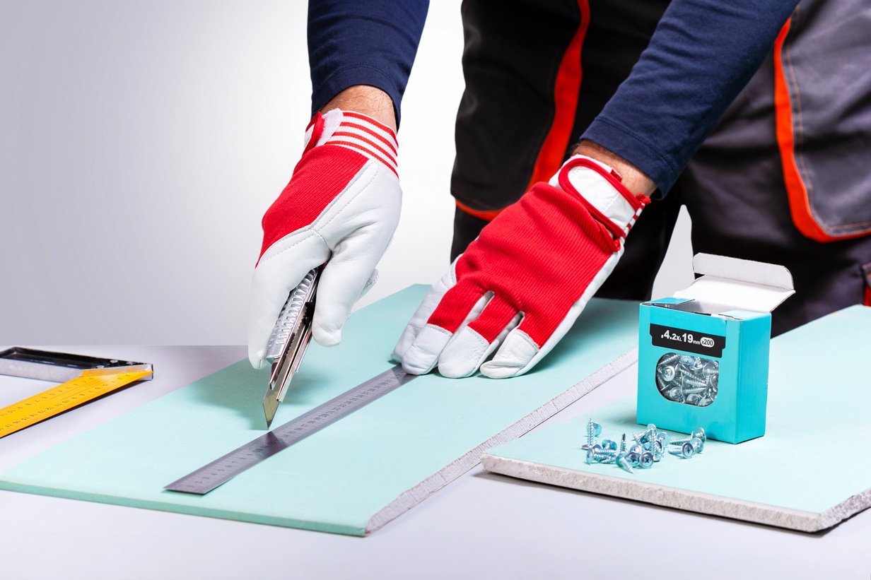 Professional builder working with drywall. Man cutting drywall with knife. Home repair concept.